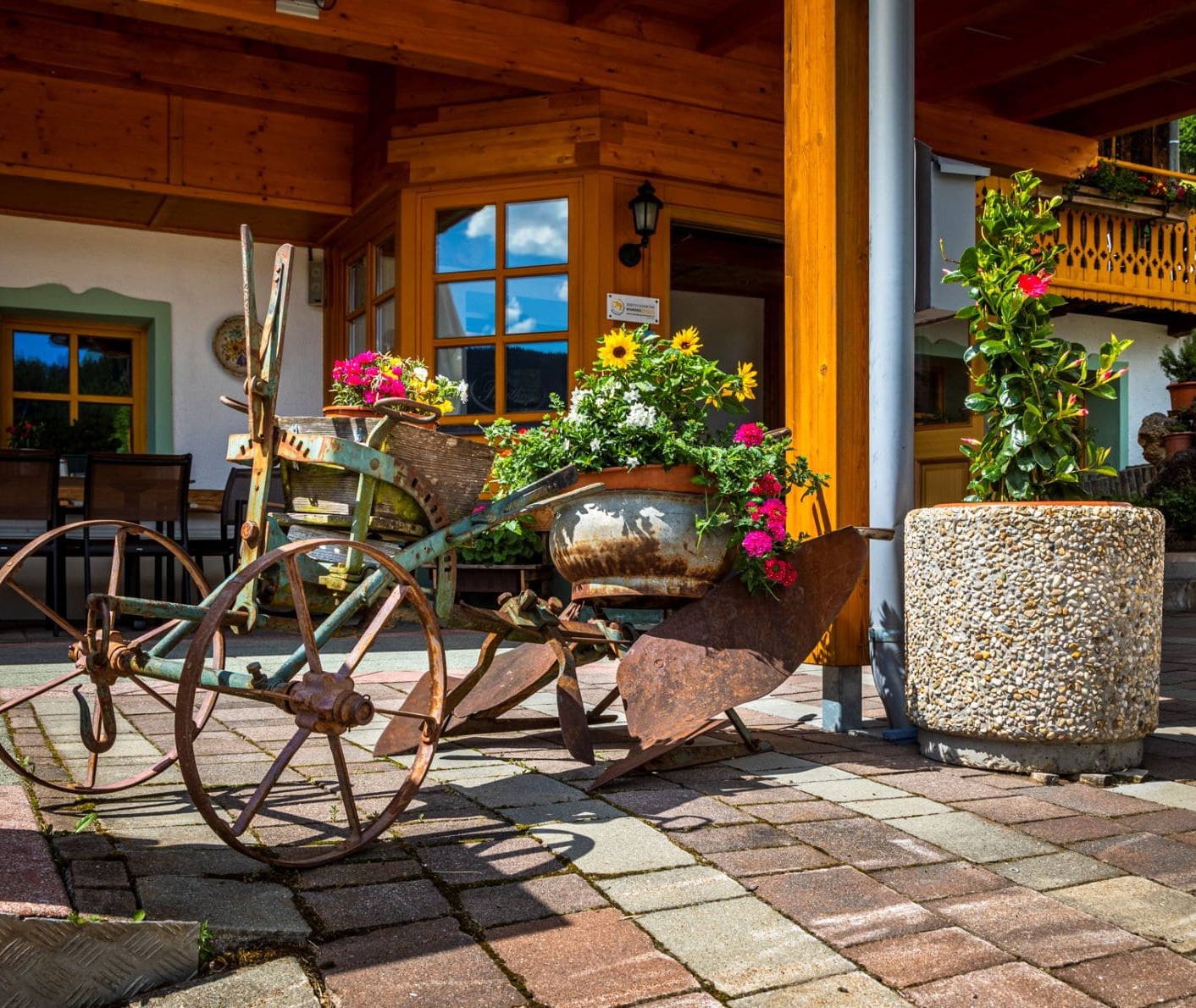 Ein alter Pflug, der mit blühenden Pflanzen dekoriert ist, lädt ein auf die Reithof Terrasse © Bernd Suppan